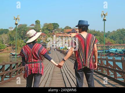 Happy Couple Walking Hand in Hand on Mon Bridge or Saphan Mon, the Iconic Landmark of Sangkhlaburi, Thailand Stock Photo