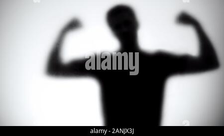Silhouette of strong man showing biceps behind glass wall, bodybuilding concept Stock Photo