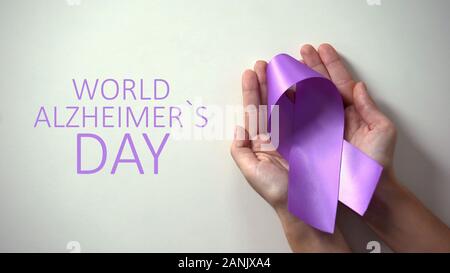 World Alzheimers day inscription, person holding purple ribbon disease awareness Stock Photo