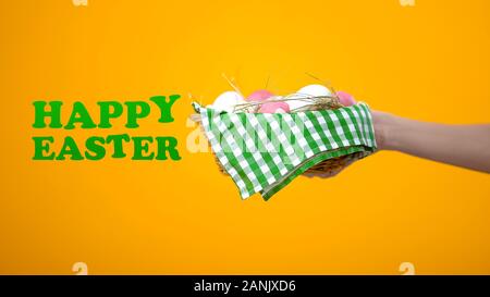 Happy Easter inscription and basket with colored eggs on yellow background, fest Stock Photo