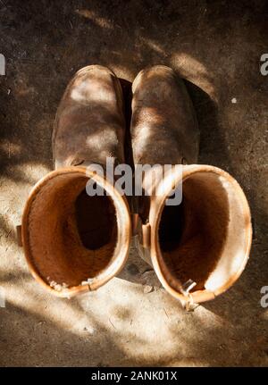 Old and used brown work boots, shot from above on a dirty shed floor Stock Photo