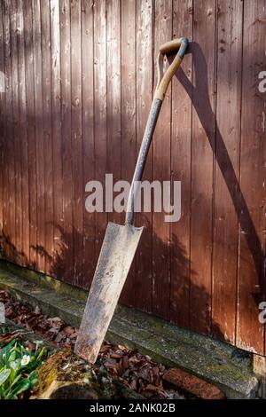 Trench or post spade leaning against an old shed wooden wall, outside in the evening sunshine. Stock Photo