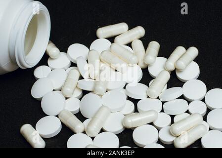 A large number of white tablets scattered from the container on a black background. concept of illness, depression, suicide. pharmaceutical pills for Stock Photo