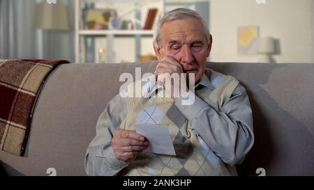 Crying elderly man looking at photo, remembering old lost friend, memories Stock Photo