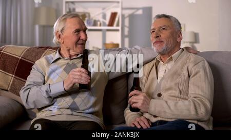 Two aged men relaxing on sofa with beer bottles, friendship communication, fun Stock Photo