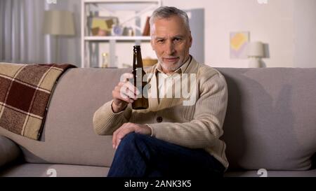 Glad retired male toasting beer bottle relaxing at home sofa, alcohol drink Stock Photo