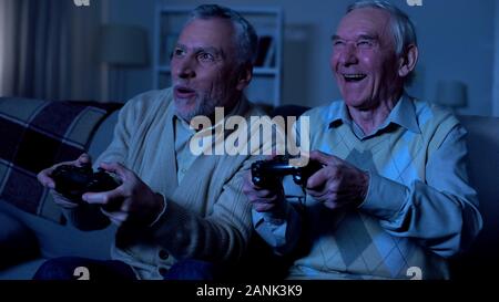 Excited retired men playing video game at night together, friendship connection Stock Photo