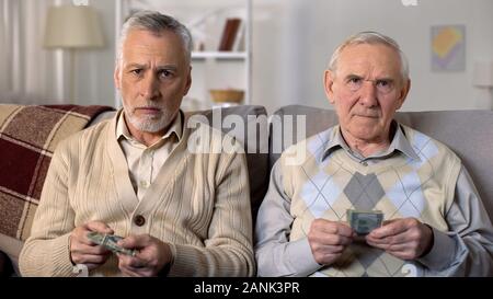 Poor retired men counting money looking sadly in camera, pension age increase Stock Photo