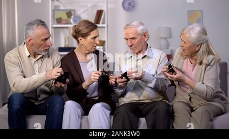 Displeased aged people showing each other empty wallet sitting nursing home sofa Stock Photo