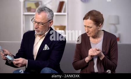 Desperate needy female looking at wealthy gentleman counting dollars, poverty Stock Photo