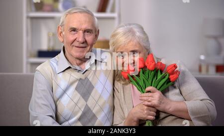 Smiling mature husband and wife with tulips looking camera, holiday celebration Stock Photo