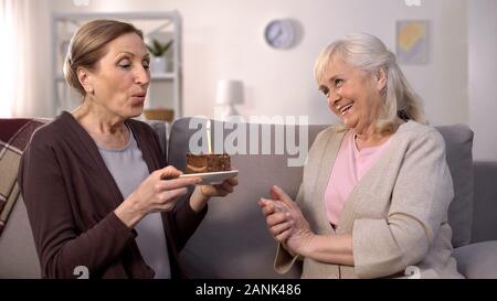 Mature woman blowing birthday cake candle sitting with smiling aged friend sofa Stock Photo