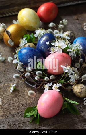 Colored Easter eggs in the nest with spring flowers on a gray wooden background. Stock Photo