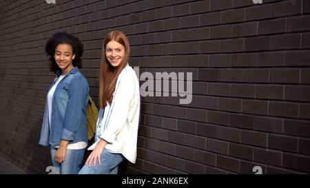 Two smiling university students leaning brick wall, leisure time college campus Stock Photo