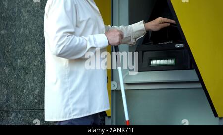 Blind man withdrawing money from atm, searching tactile indicator to insert card Stock Photo