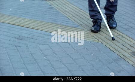 Blind man finds turn on tactile paving using walking stick, urban navigation Stock Photo