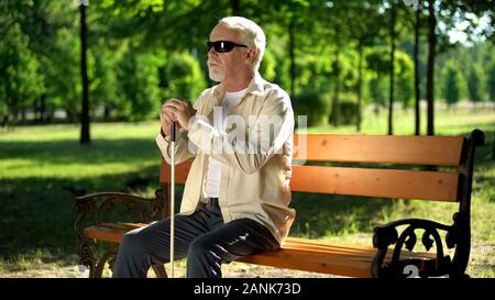 Blind man sitting on bench, listening for sounds in park, heightened senses Stock Photo