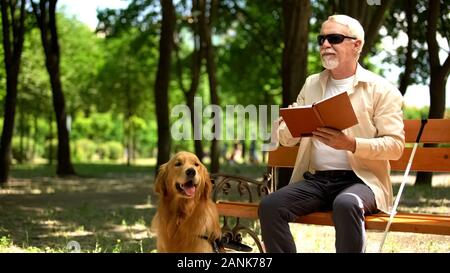 Blind man feels happy reading book, resting with dog, socially secure life Stock Photo