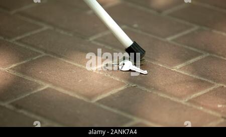 Blind man searching key using cane, outdoor difficulties experienced by impaired Stock Photo