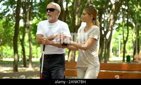 Kind girl helping blind pensioner to sit on bench, respect and care for disabled Stock Photo