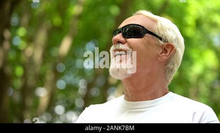 Visually impaired man in sunglasses listening nature sounds, heightened senses Stock Photo