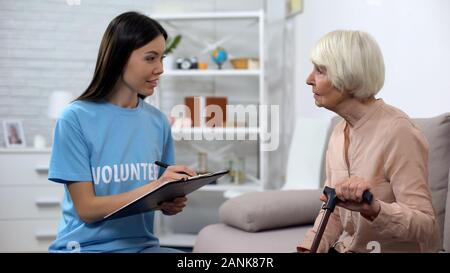 Young activist making list listening to aged lady walking stick, nursing home Stock Photo