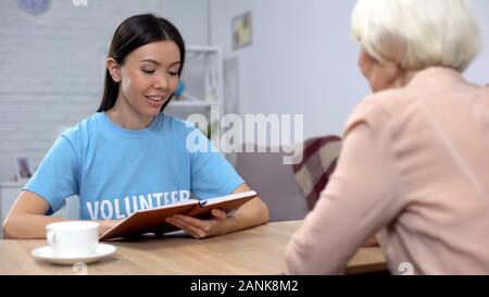 Smiling social worker reading book senior retired lady, generations togetherness Stock Photo