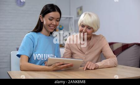 Social carer showing tablet application to senior female pensioner, support Stock Photo