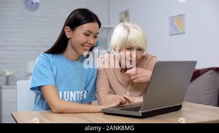 Nursing home volunteer teaching aged lady to use laptop, online app, technology Stock Photo