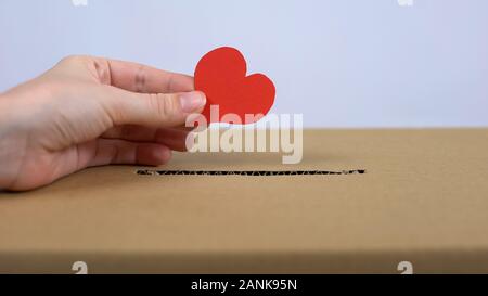 Female hand putting red heart sign in cardboard box, donation center, medicine Stock Photo