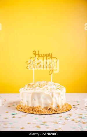 Birthday cake with golden topper. Birthday party celebration concept. Vertical, bold yellow background Stock Photo