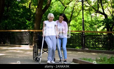 Young woman helping old lady walking on crutches, hip fracture rehabilitation Stock Photo