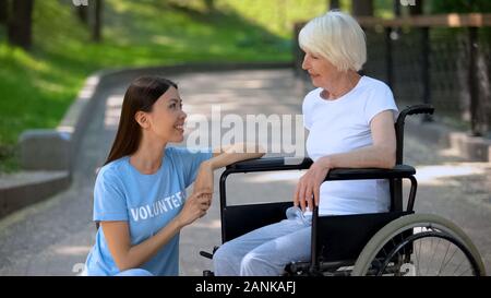 Disabled senior lady in wheelchair smiling to volunteer, communication support Stock Photo