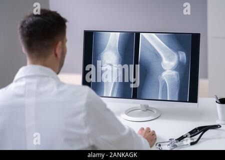 Mature Male Doctor Examining Knee X-ray In Clinic Stock Photo