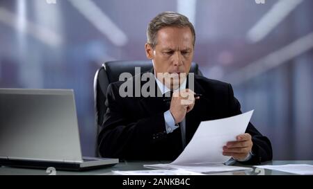 Serious businessman reading important contracts at office desk, agreement Stock Photo