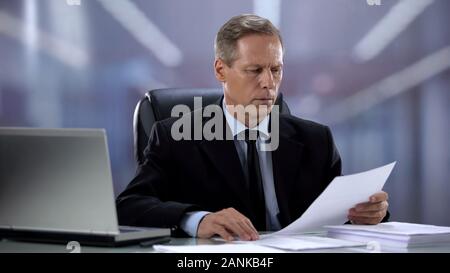 Head of company checking reports, attentively reading documents at office desk Stock Photo