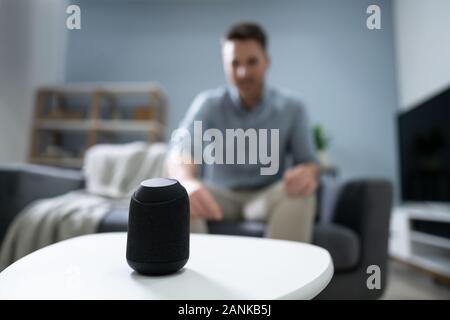 Close Up Of Wireless Speaker In Front Of Man Sitting On Sofa Stock