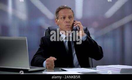 Angry boss in suit screaming cellphone on worker displeased with failed contract Stock Photo