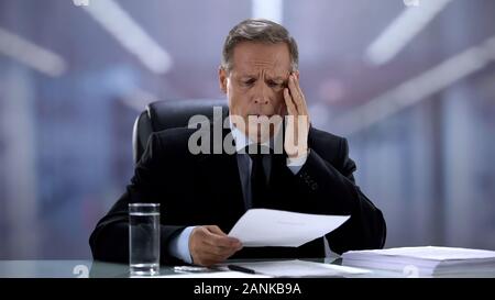Tired business person suffering migraine reading document, strong headache Stock Photo