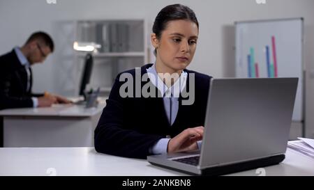 Tired female office worker typing on laptop, overworking concept, exhaustion Stock Photo