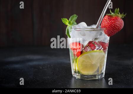 Detox lemonadeor mojito with lime and strawberry in rocks glass. Summer healthy freshness drink. Horizontal orientation. Dark wooden background. Space Stock Photo