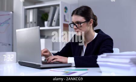Female office worker typing on computer, looking responsible and focused on task Stock Photo