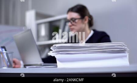 Pile of papers on office table, female employee working on background, workload Stock Photo