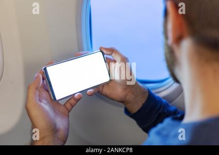 Mockup smartphone airplane. Young attractive european man holding blank screen smartphone in hands in airplane. Mock up for a game, mobile application Stock Photo