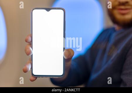 Mockup smartphone airplane. Young attractive european man holding blank screen smartphone in hands in airplane. Mock up for a game, mobile application Stock Photo