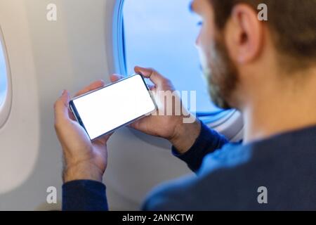 Mockup smartphone airplane. Young attractive european man holding blank screen smartphone in hands in airplane. Mock up for a game, mobile application Stock Photo