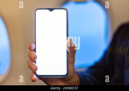 Mockup smartphone airplane. Young attractive european man holding blank screen smartphone in hands in airplane. Mock up for a game, mobile application Stock Photo