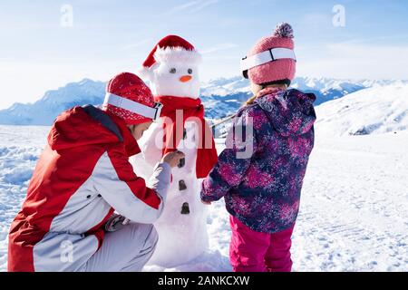 Mother With Her Daughter Playing In Fresh Snow And Making Snowman On Beautiful Winter Day Stock Photo