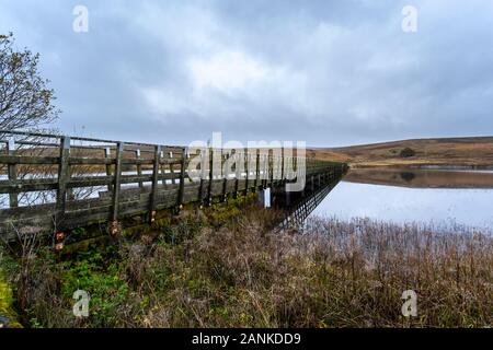 A moss and Lichen covered footbridge crosses over the water, Alwen reservoir, North Wales Stock Photo