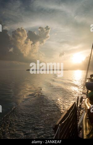 Sailing through the gulf of mexico on boat with sunset and few clouds above horizon. Sea water reflecting sun, side of boat visible. No people, copysp Stock Photo